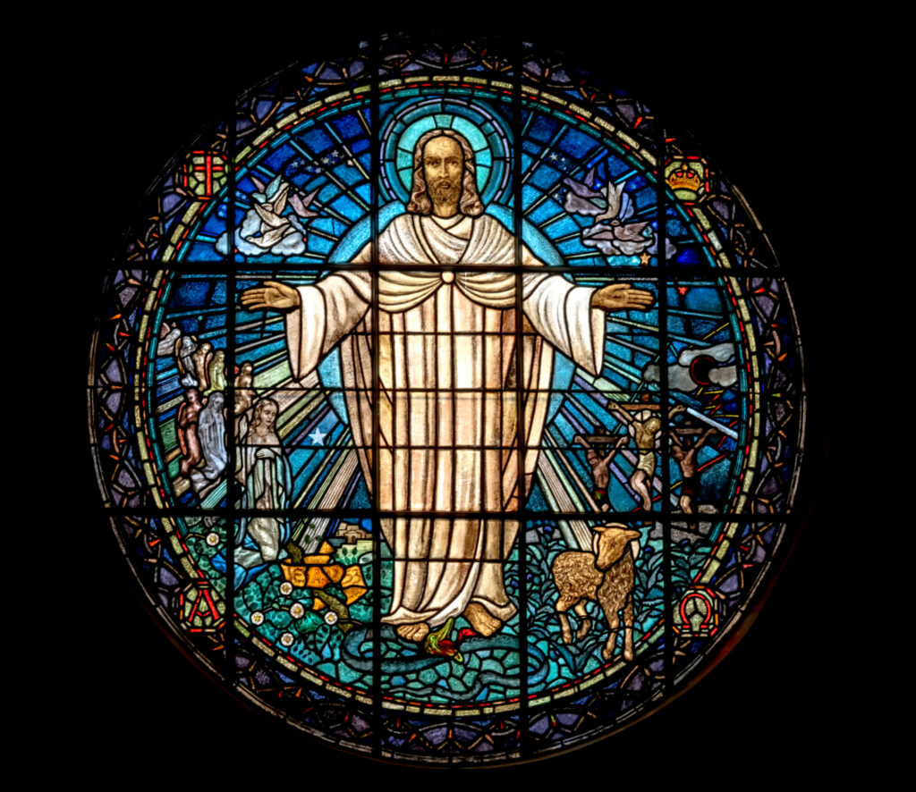 Vidriera de una iglesia representando a Cristo con los brazos abiertos, rodeado de palomas